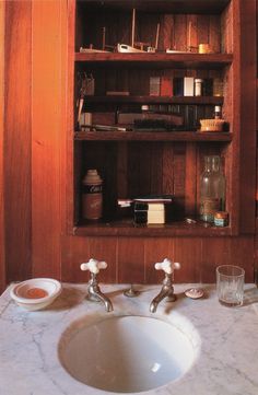 a bathroom sink with two faucets in front of a wooden book shelf filled with books