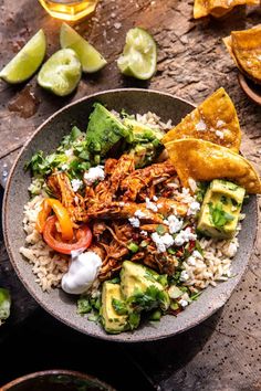 a bowl filled with rice, meat and vegetables next to tortilla wedges