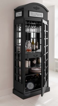 a black phone booth with liquor bottles and glasses on it's shelves in a white room