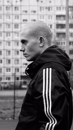 a man with a bald head standing in front of a tall building wearing a black jacket