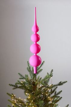 a pink christmas tree with three balls on top and lights in the bottom, against a gray background