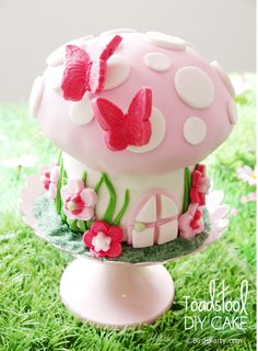 there is a cake that looks like a mushroom on the grass with flowers and butterflies