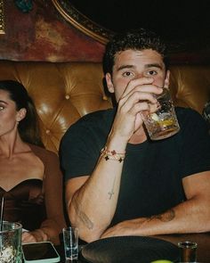 a man sitting at a table drinking from a glass in front of two other people