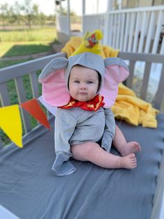 a baby wearing an elephant costume sitting on top of a crib in the yard