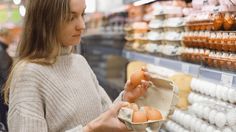 a woman holding an egg in a carton while looking at eggs on the shelf