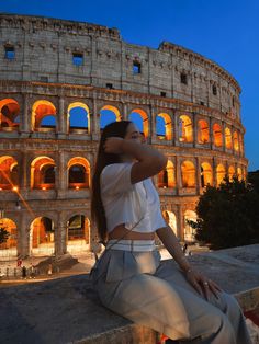 a woman sitting in front of the colossion at night with her hands behind her head