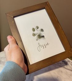 a person holding up a frame with a dog's paw prints on it and the word jesus written in cursive writing