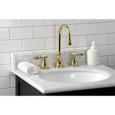 a bathroom sink with gold faucet and marble counter top next to white tile