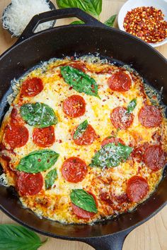 a pizza in a skillet with basil and pepperoni on top, next to other ingredients