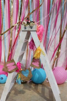 a ladder decorated with pink, blue and yellow paper flowers sits in front of streamers