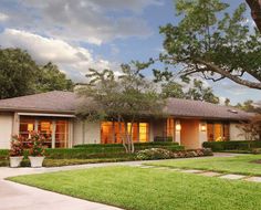 a house that is in the middle of some grass and trees with bushes around it