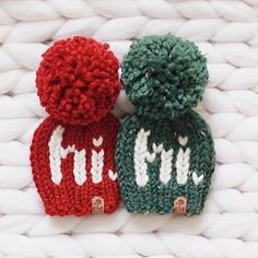 two knitted hats sitting next to each other on top of a white cloth surface