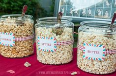 three glass jars filled with popcorn sitting on top of a red tablecloth covered table