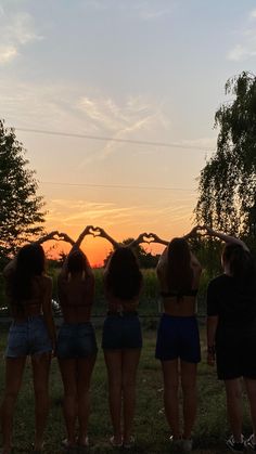 four girls are standing in the grass with their backs turned to the camera as the sun sets