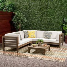 an outdoor living area with white couches and green plants on the wall behind it