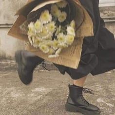 a person wearing black boots and holding a bouquet of daisies