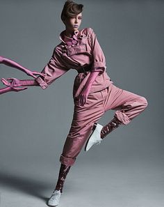 a woman in pink jumpsuits and white shoes with her arms spread out to the side