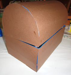 an open cardboard box sitting on top of a white table covered in blue tape and other items