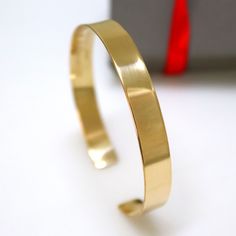 a close up of a gold bracelet on a white surface with a red object in the background