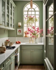 a kitchen with green cabinets and pink flowers in vases on the window sill