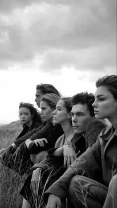 a group of people sitting on top of a grass covered field next to each other