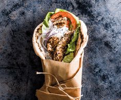 a burrito wrapped in brown paper with lettuce, tomato and chicken on top