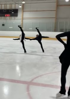 three people are skating on an ice rink and one person is holding their arms up