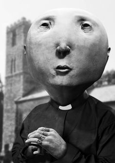 a person with a large head wearing a priest's outfit and holding a small hand