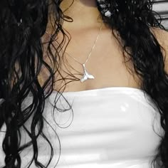 a woman with long black hair wearing a white top and silver necklace on her neck