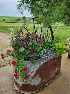 an old rusty barrel filled with flowers and greenery next to a bench in a park