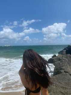 a woman standing on top of a sandy beach next to the ocean under a blue cloudy sky