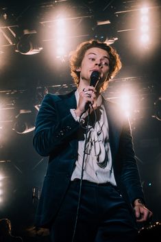 a man holding a microphone up to his mouth while standing in front of spotlights