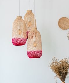 three hanging lights made out of straw and pink yarn on the wall next to dried flowers