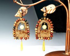 Our Timekeeper Earrings mimic the facade of the vintage cuckoo clock. They are hand embroidered with gold Japanese beads, framed with Picasso Jasper Stones, with dangling round yellow Jade stones in the windows, and dangling lime yellow dyed Quartz stone teardrops as pendulums. This unique showpiece is part of our Cuckoo Clock Collection. Bohemian Jeweled Beaded Earrings For Gifts, Clock Collection, Lucky Jewelry, Lime Yellow, Japanese Beads, Casual Earrings, Yellow Quartz, Gold Bodies, Yellow Jade