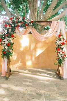 an outdoor wedding setup with flowers and draping on the wall, in front of a large tree