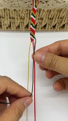 two hands are working on an ornament with red, yellow and green thread