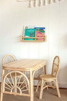 two chairs and a table with books on the shelf above them in a white room