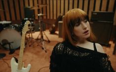 a woman with red hair and bangs standing in front of a drum set, looking at the camera