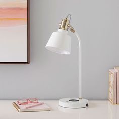 a white desk lamp sitting on top of a table next to a pink and yellow painting