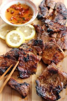 chopsticks and meat on a cutting board with lemon wedges