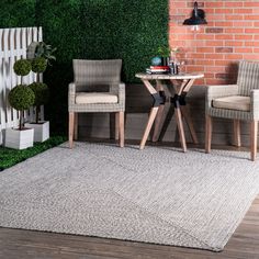 two chairs and a table in front of a brick wall with grass growing on it