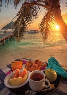 a plate with some fruit on it next to the ocean and a palm tree at sunset