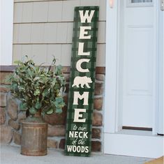 a welcome sign sitting next to a potted plant on the side of a house