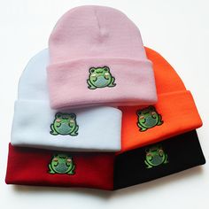 three beanies with frog embroidered on the front and two are red, one is pink, one is green