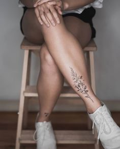 a woman sitting on top of a wooden chair with her legs crossed and flowers tattooed on the leg