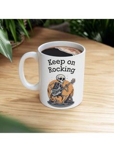 a coffee mug with the words keep on rocking and a skeleton playing an electric guitar