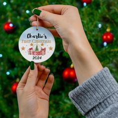 a person holding up a christmas ornament in front of a christmas tree