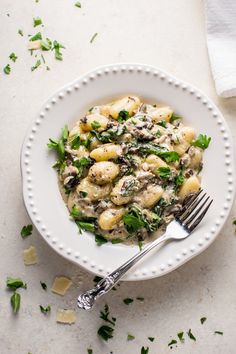 a white bowl filled with pasta and spinach covered in sauce on top of a table