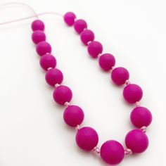 a pink necklace on a white surface with a string attached to it and beads in the shape of balls