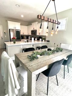 a dining room table with chairs and lights hanging from it's ceiling in front of an open kitchen